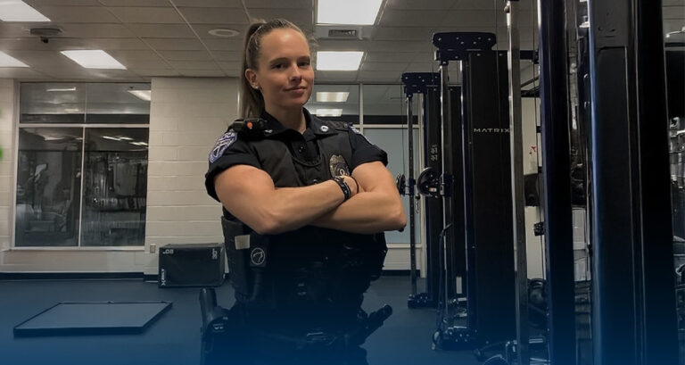 Meredith Ketcher, female member of law enforcement, stands in uniform in the Gordon College Bennett Center weight room.